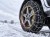 Grafika AI: Koło auta z łańcuchami śniegowymi Campcar KNS 100 9 mm na zaśnieżonej drodze - Sklep motozebra