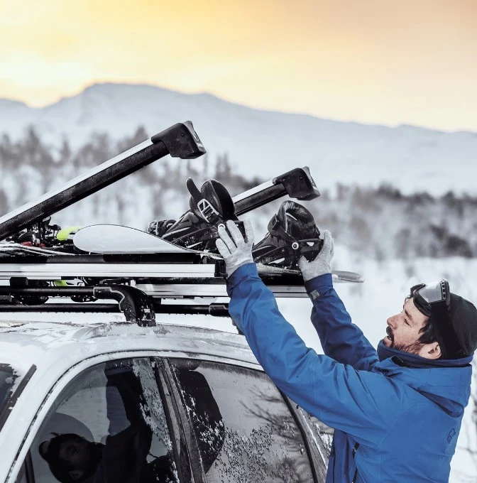 Narciarz w rękawicach wkłada deskę snowboardową do otwartego uchwytu Amos Ski Lock na dachu auta zimą