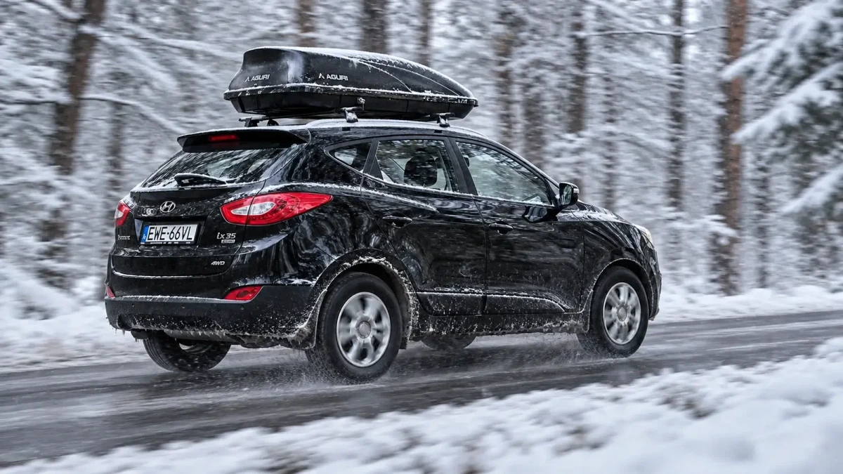 Czarny SUV z czarnym boxem dachowym jedzie zimą ośnieżoną drogą przez zaśnieżony las - Sklep motozebra